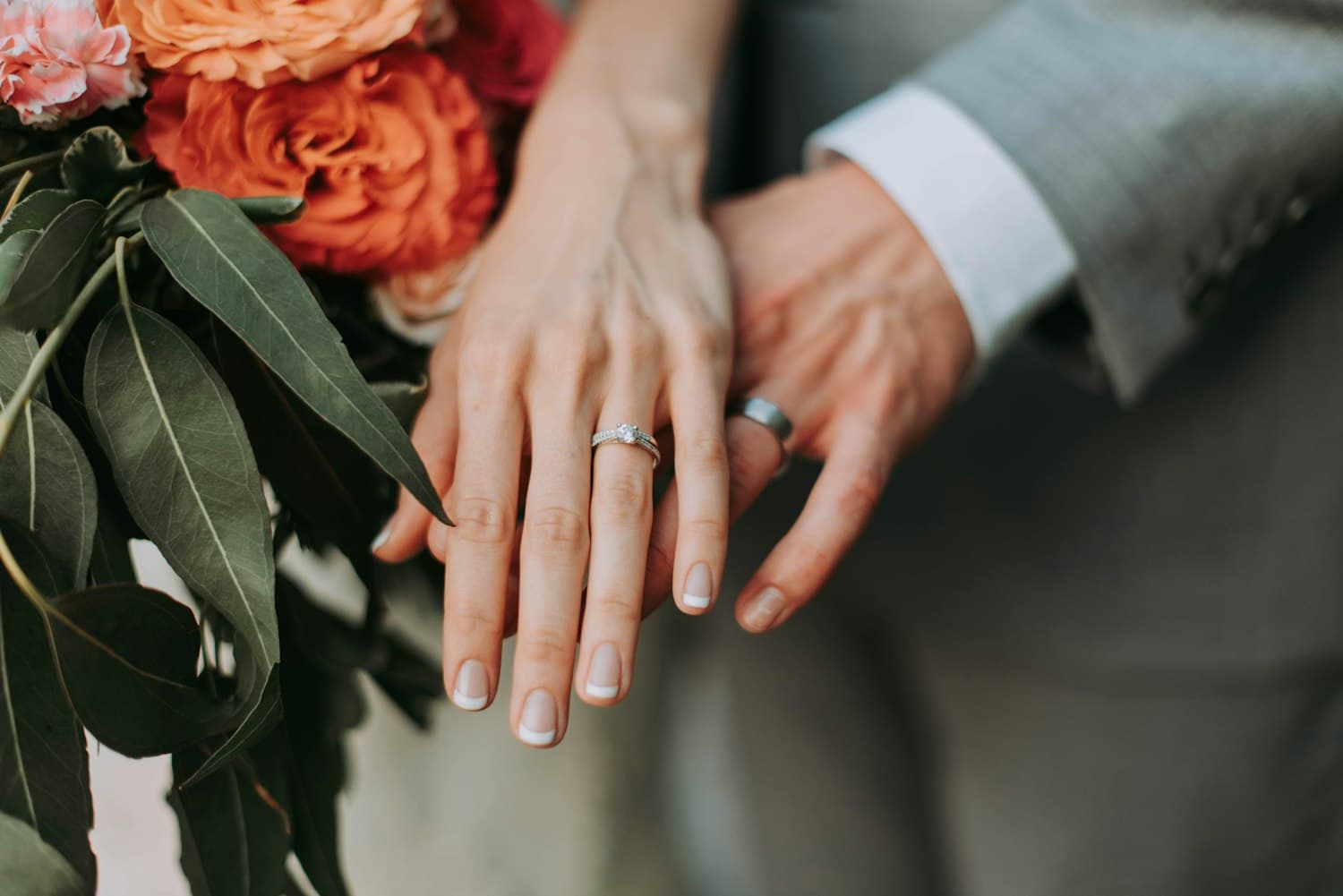 Two hands resting together, both wearing rings, beside cut flowers