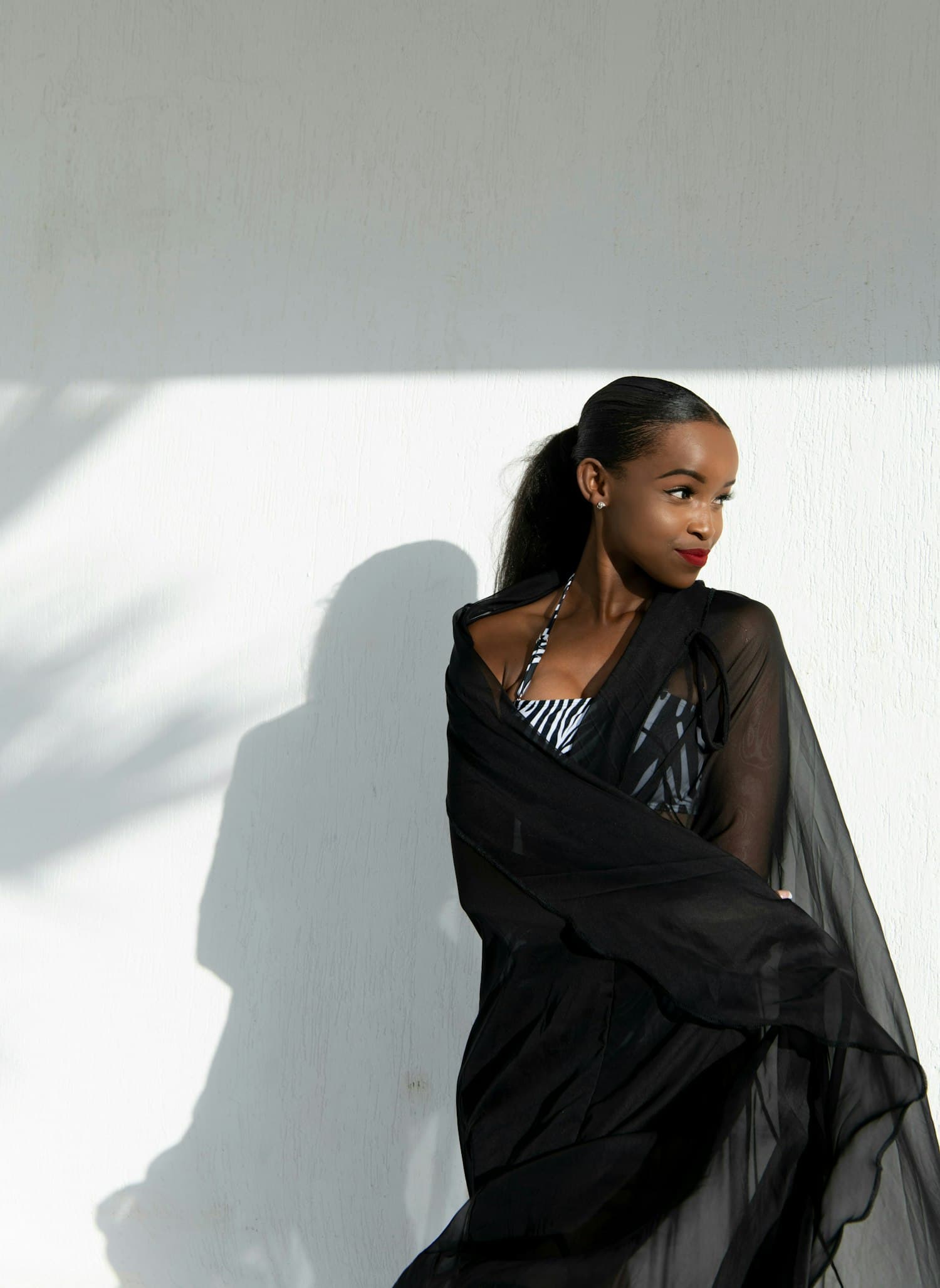 A woman in a black shawl against a white wall, hard shadow behind her