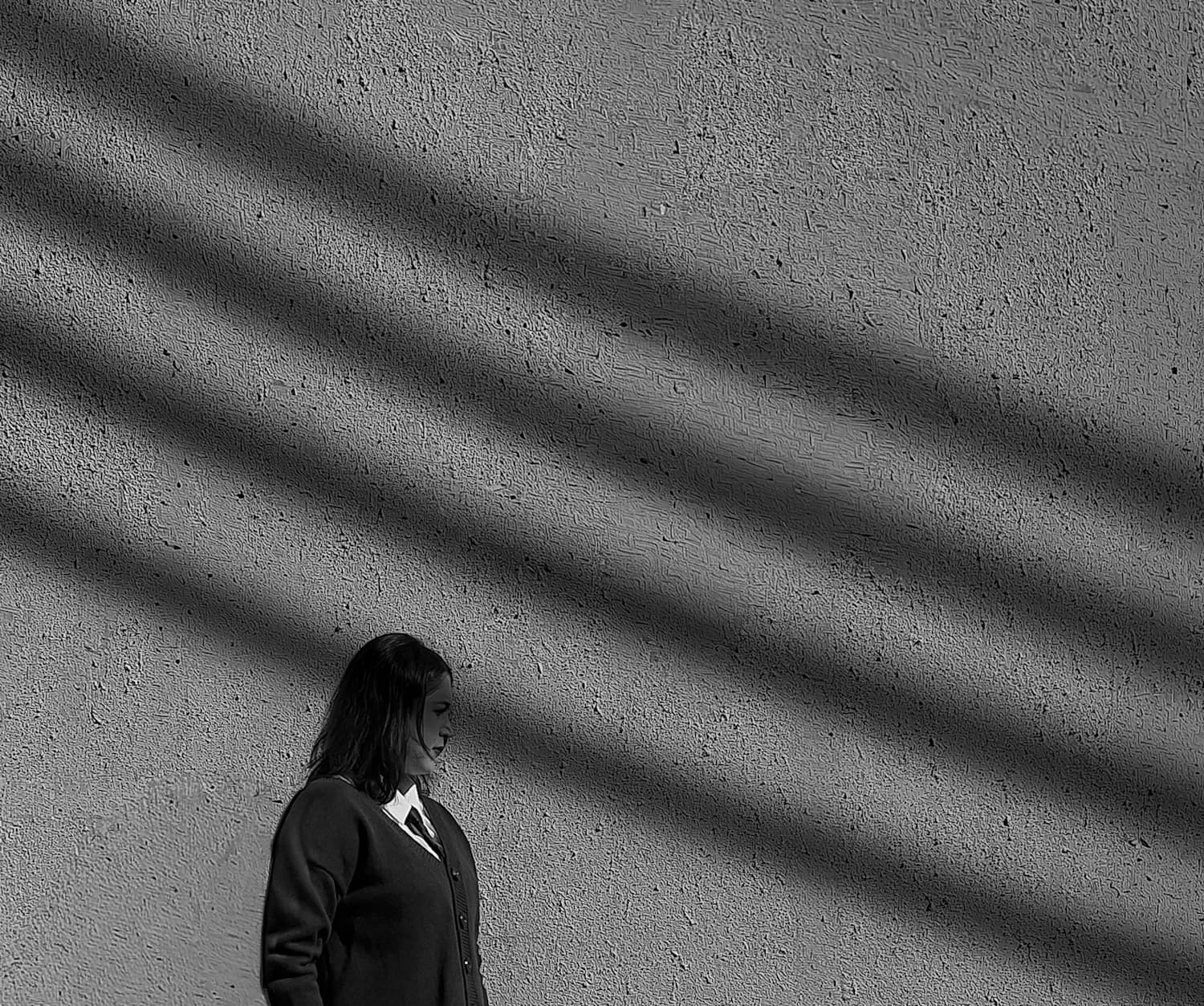A figure crossing textured concrete, cut across by diagonal shadow