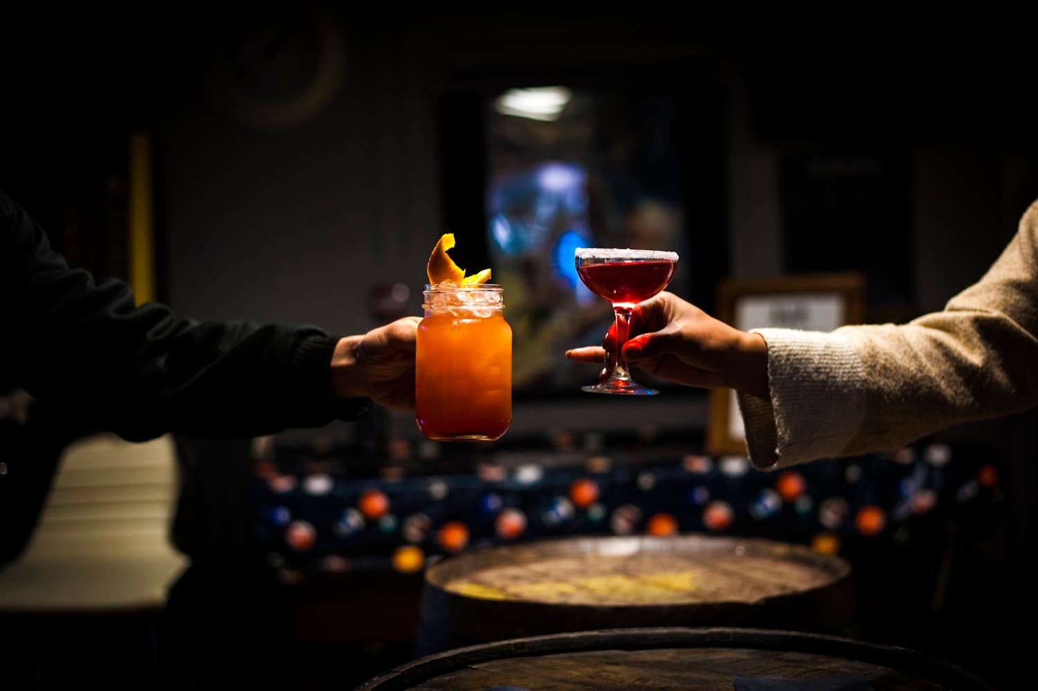 Two hands touching cocktail glasses together in a dark room